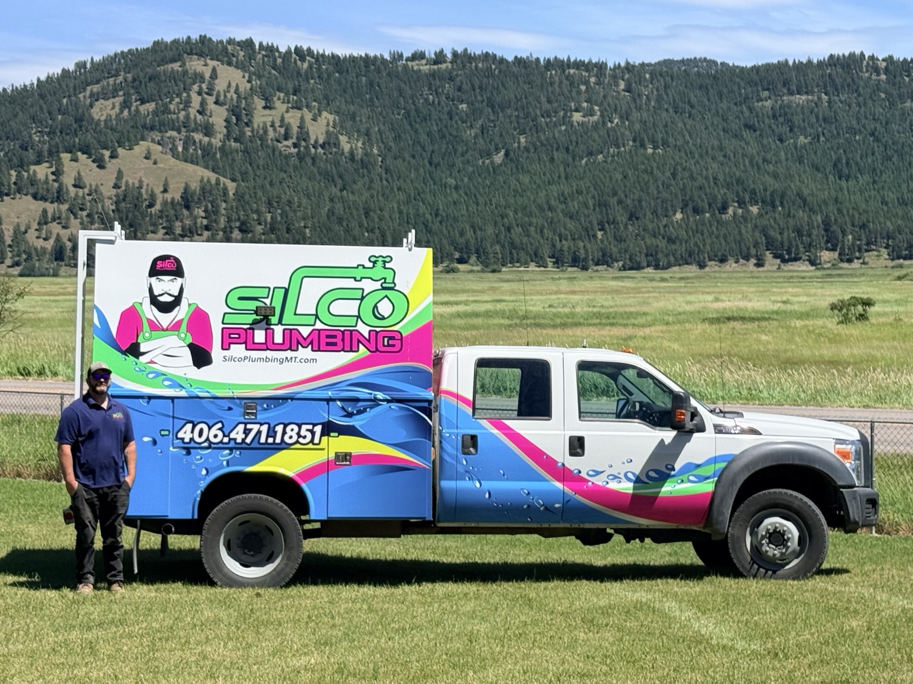 The owner of Silco Plumbing beside his wrapped service truck, Montana mountains behind, Kalispell.